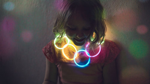 Close-up of girl wearing illuminated necklace against wall