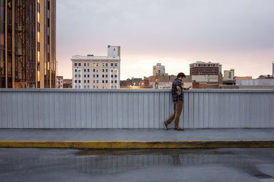 Side view of man standing on bridge with mobile phone against sky