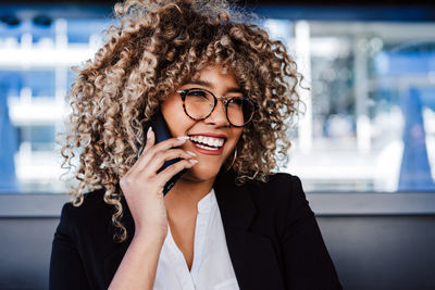 Smiling hispanic afro business woman wearing eye glasses in cafe using laptop and mobile phone