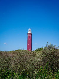 Lighthouse by sea against clear blue sky