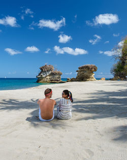 Rear view of woman sitting on beach against sky