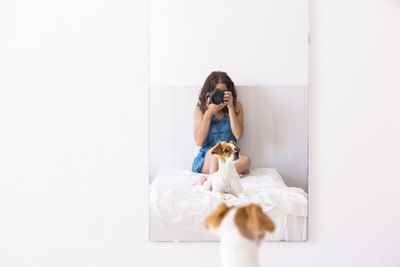 Reflection of woman photographing by dog in mirror at home