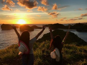 Rear view of friends standing at beach against sky during sunset