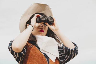 Young woman looking through binoculars against white background