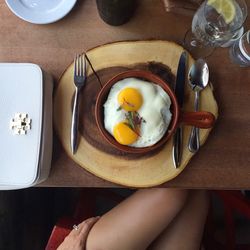 Cropped image of woman sitting by table with fried egg and refreshment in restaurant