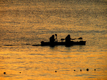 Silhouette people swimming in sea against sky during sunset