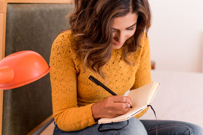 Smiling woman writing in diary while sitting on bed at home