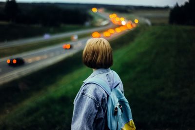 Woman standing with backpack against road at dusk