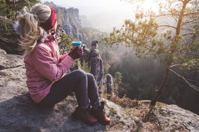 Full length of woman sitting on rock while looking at view