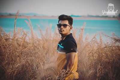 Young man wearing sunglasses standing by sea against sky