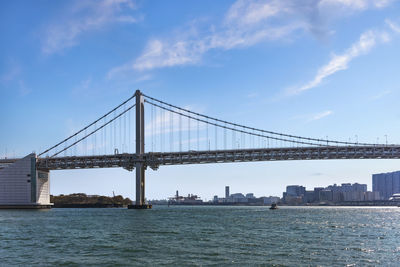 Double-layered suspension rainbow bridge in tokyo bay with the gantry cranes of the port of tokyo.