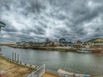 Buildings by river against cloudy sky