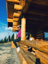 Low angle view of woman wearing sunglasses sitting on wooden railing
