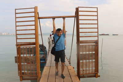 A young asian man standing arms up in an open lattice door on a narrow wooden pier in george town.