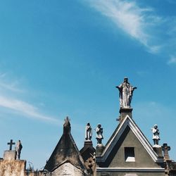 Low angle view of sculptures at cemetery against sky