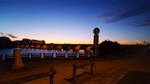 Empty benches by sea against clear sky at sunset