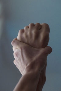 Close-up of person hand holding leg against blue wall
