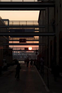 People walking on illuminated street amidst buildings in city at sunset