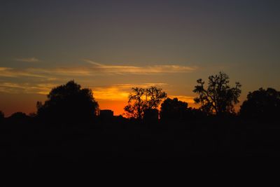 Silhouette trees on landscape against sky at sunset