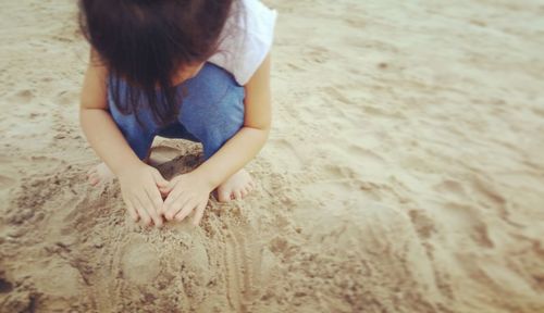 High angle view of girl playing while crouching on sand