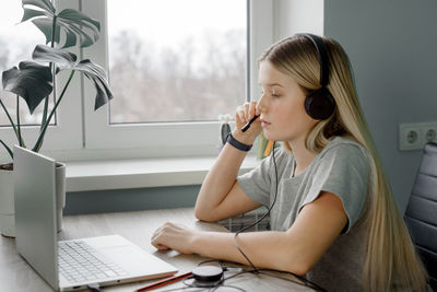 Teenage student girl in headphones having online lesson at home