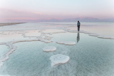 Young woman standing on salt formations in dead sea at sunset