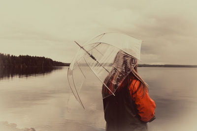 Woman holding umbrella while standing by lake