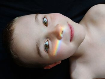 Close-up portrait of shirtless boy with rainbow against black backdrop