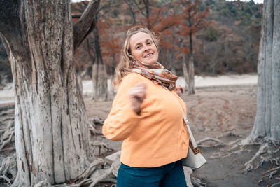 Woman standing by tree trunk in forest