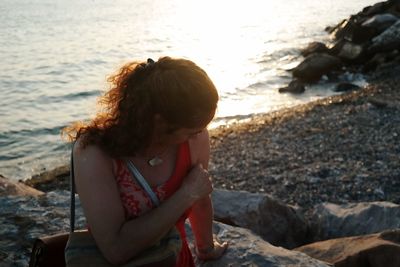 Mature woman sitting on rock at beach during sunset