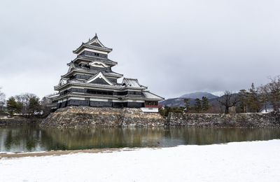 Traditional building by lake against sky during winter