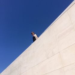 Low angle view of man standing on building terrace against clear blue sky