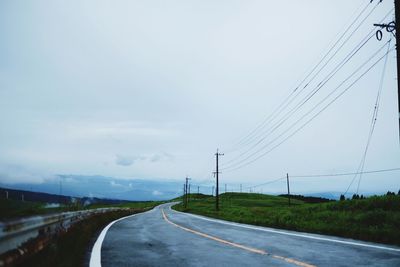 Road by electricity pylon against sky