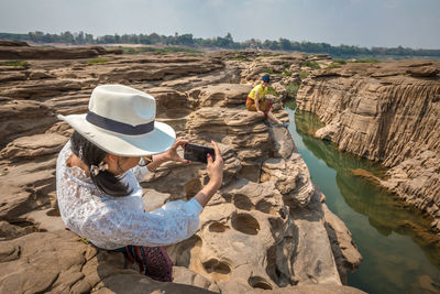 Rear view of man photographing woman on rock