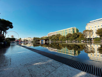 Reflection of buildings in river against clear blue sky