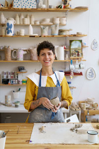 Happy self-employed pottery artist woman in creative studio work with raw clay shaping handmade cup