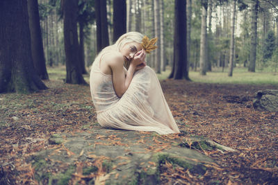 Portrait of young woman relaxing with autumn on rock in forest