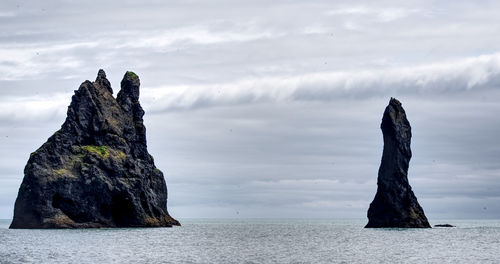 Rock formations in sea against cloudy sky