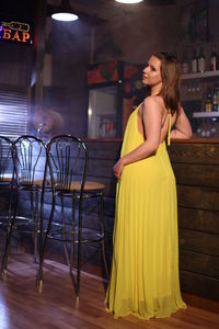 Smiling young woman standing against yellow wall at night