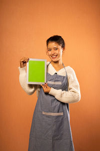 Portrait of young woman using digital tablet while standing against yellow background