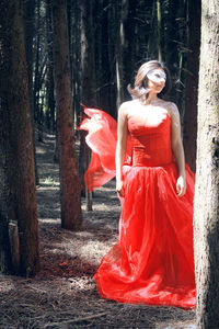 Woman in red dress standing by trees in forest