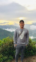 Portrait of young man standing on mountain against sky