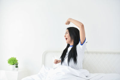 Young woman yawning against wall on bed at home