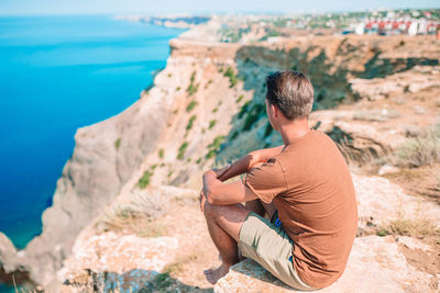 Rear view of man sitting on rock