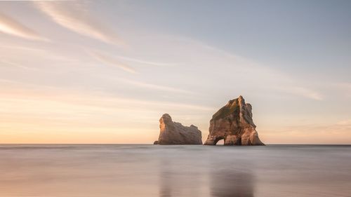 Rock formation in sea against sky during sunset