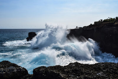 Waves splashing on rocks against sky