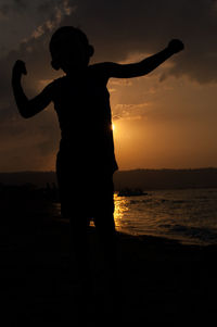 Silhouette boy standing on beach against sky during sunset