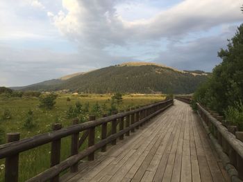 View of wooden bridge on landscape against sky