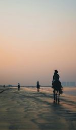 People walking on beach against sky during sunset