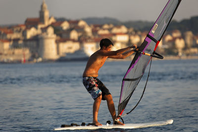 Full length of shirtless man standing on sea against sky